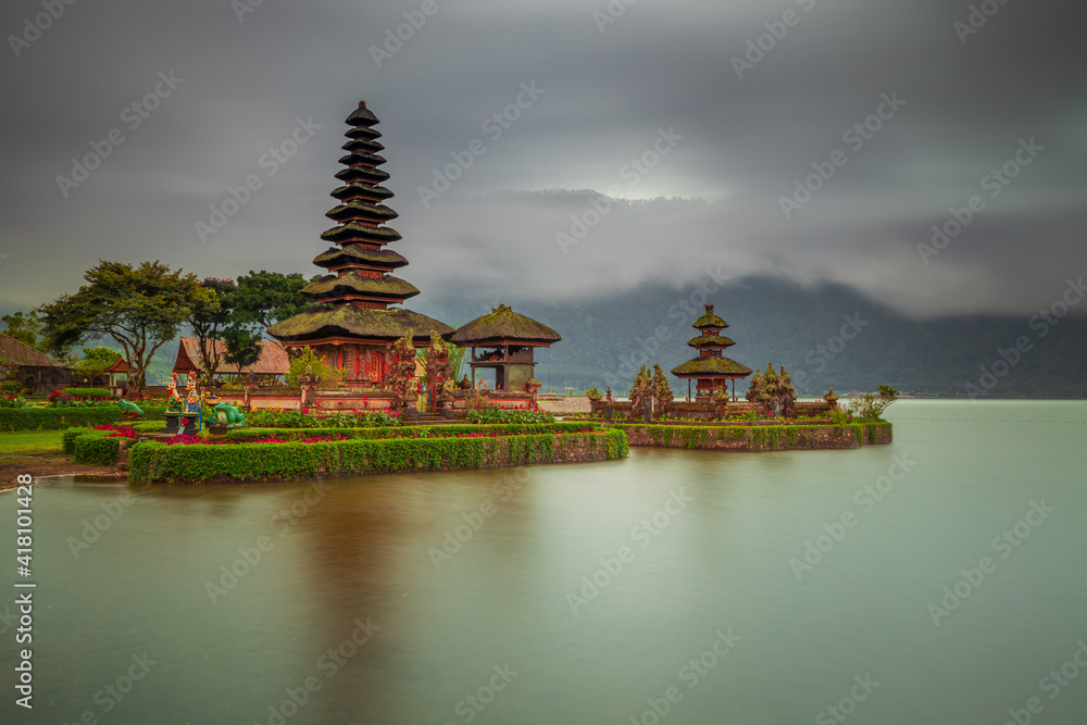 Naklejka premium Pura Ulun Danu Bratan temple in Bali island. Beautiful balinese temple during sunrise. Balinese landmark. Cloudy sky. Water reflection. Slow shutter speed. Bratan lake, Bali