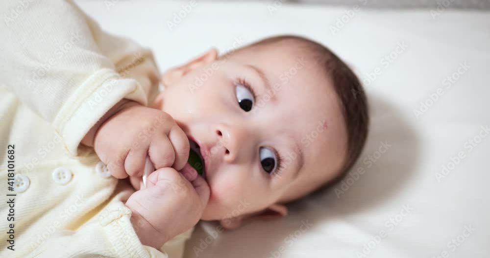 Newborn cheerful littlebaby is chewing and playing in his crib with nipple. Funny smiling looks through the railing of the crib. slow motion Newborn cheerful littlebaby is chewing and playing in his crib with nipple. Funny smiling looks through the railing of the crib. slow motion