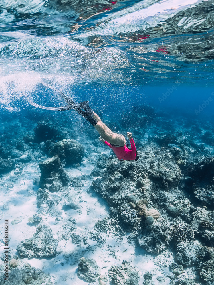 Woman with fins glides over corals, snorkeling in clear ocean.