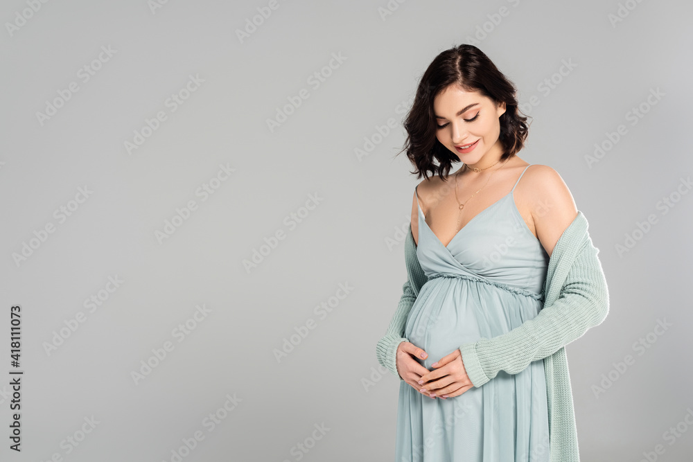 Smiling pregnant woman looking at belly isolated on grey Smiling pregnant woman looking at belly isolated on grey