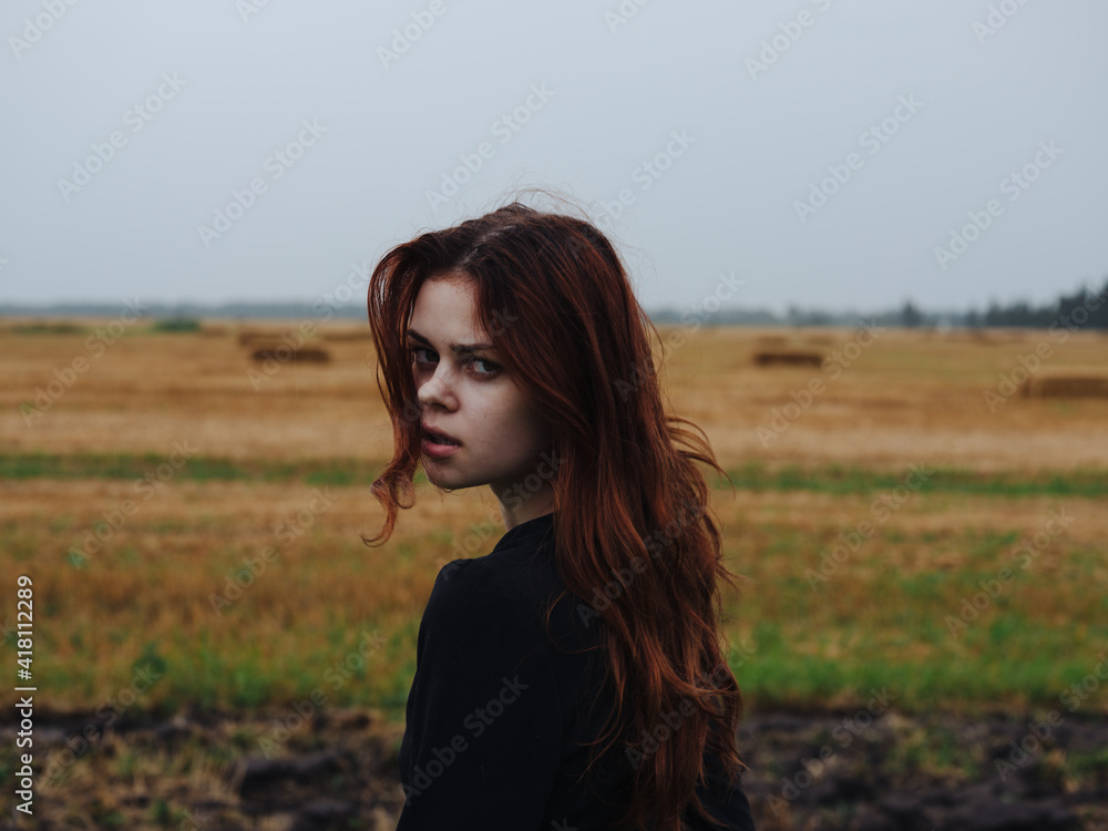 Portrait of a red-haired woman in a black dress in a field in nature cropped view Portrait of a red-haired woman in a black dress in a field in nature cropped view
