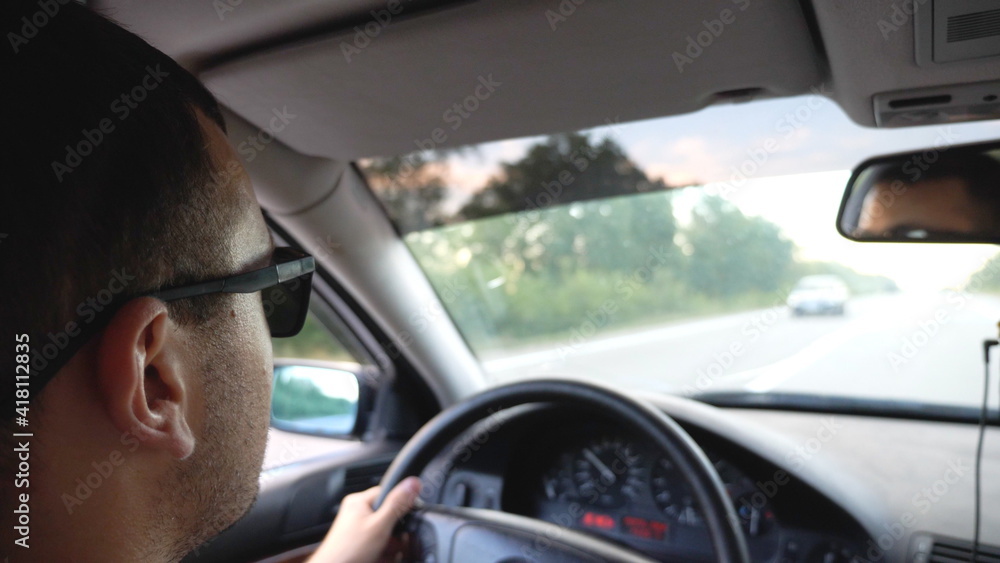 Unrecognizable man in sunglasses driving car on highway. Young confident guy looking to road during controlling auto. Back view from vehicle salon. Concept of road trip. Slow motion Unrecognizable man in sunglasses driving car on highway. Young confident guy looking to road during controlling auto. Back view from vehicle salon. Concept of road trip. Slow motion
