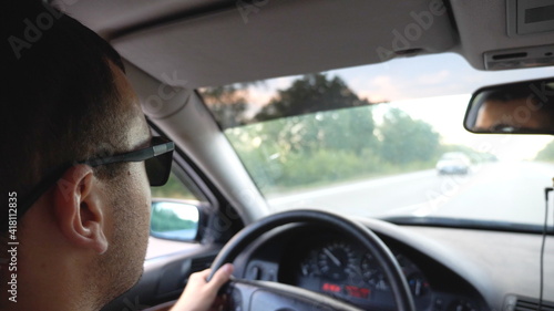 Unrecognizable man in sunglasses driving car on highway. Young confident guy looking to road during controlling auto. Back view from vehicle salon. Concept of road trip. Slow motion © olehslepchenko