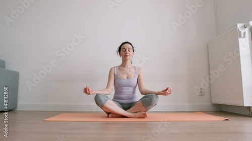 Woman sits in lotus position with closed eyes on yoga mat at home © kristinakibler