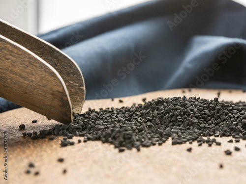 Black kumin seeds on a wooden cutting board and blue napkin.   Wooden spoon and black kumin seeds  . Superfoods.  Immunity support, vitamins and supplements .  Oriental recipes of healthy life.   photo