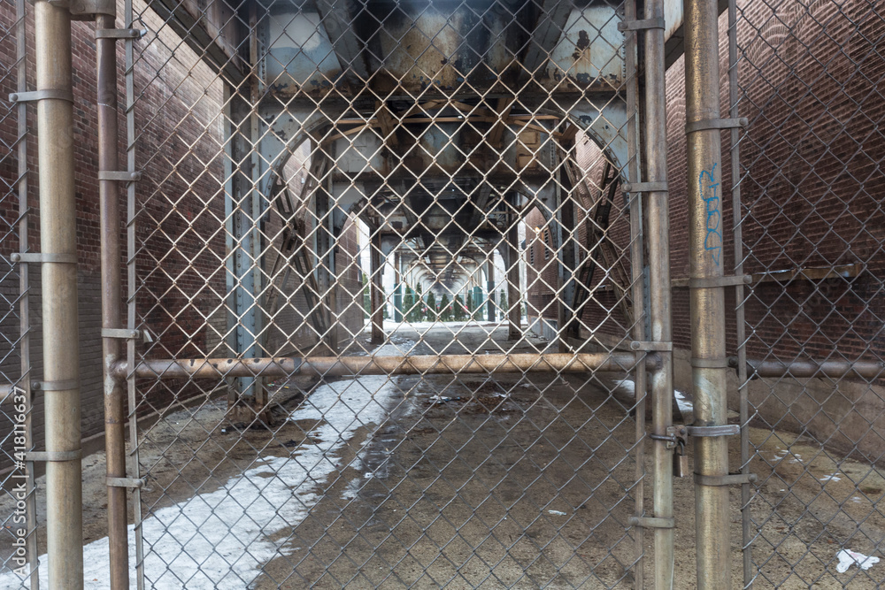 Looking through urban fencing to overhead elevated subway tracks cutting through alleyway in urban Chicago