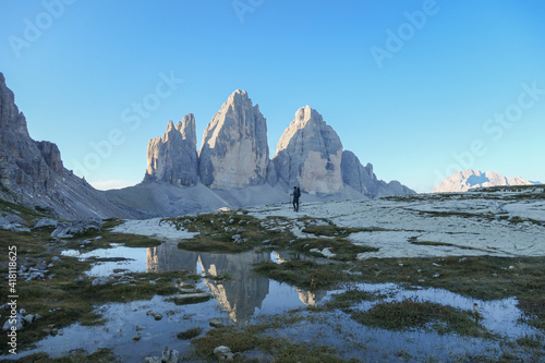 A man hiking with the view on the Tre Cime di Lavaredo (Drei Zinnen), mountains in Italian Dolomites. The mountains are reflecting in small paddle. Desolated and raw landscape. Early morning. Daybreak