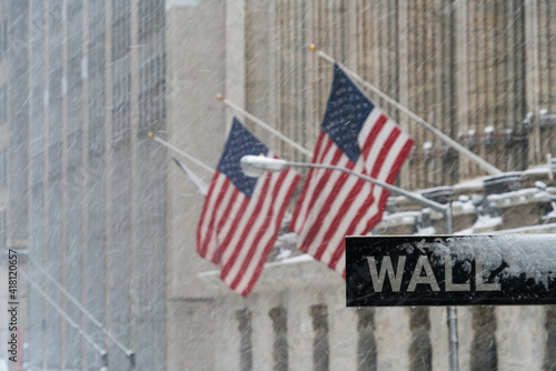 Wall Street road sign stands at front of New York Stock Exchange during the winter snowstorm at Lower Manhattan New York City NY USA.