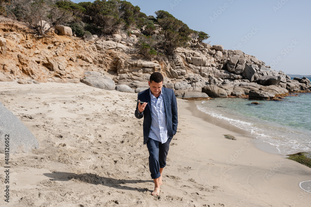 Businessman with suit walking on the beach holding a smartphone listening a vocal message.