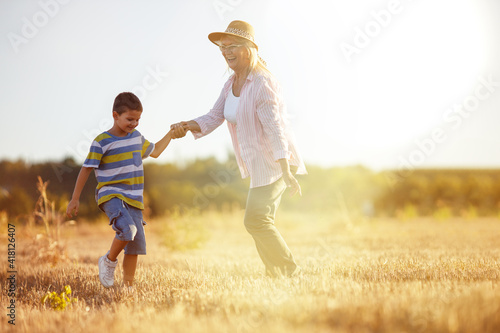Grandmother walking on the meadow with her grandson. Relaxing and joying in sunset. 