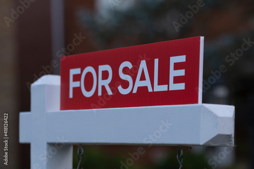 New red sign for sale in front of house in residential area. Real estate bubble, bidding war, hot housing market, overpriced property, buyer activity, spring and summer sale concept. Selective focus.
