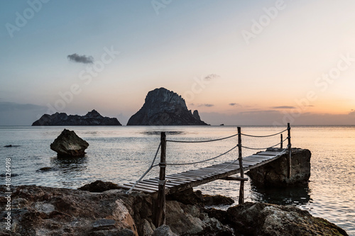 Amazing sunset light over Es Vedrá in Ibiza from a wooden structure on the shore. photo