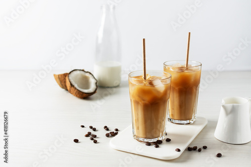 Iced coffee with coconut milk in a tall glass on white wooden table.