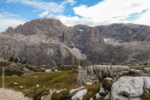 Panoramic view on the valley in Italian Dolomites. The bottom of the valley is overgrown with small plants. In the back there is a high mountain chain, with very sharp slopes. Serenity and recharging