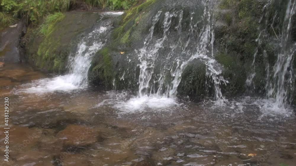 Beautiful waterfall in rainforest. Few jets of water fall in small pond. Mountain river flows down mossy boulders. Green vegetation on bank of spring. In lake can see stones through waves at bottom Beautiful waterfall in rainforest. Few jets of water fall in small pond. Mountain river flows down mossy boulders. Green vegetation on bank of spring. In lake can see stones through waves at bottom