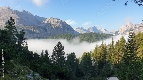 An early morning in Italian Dolomites. A thick forest overgrowing the area. The valley is shrouded in morning haze. There are high, stony mountain chains around. Golden hour. New day beginning