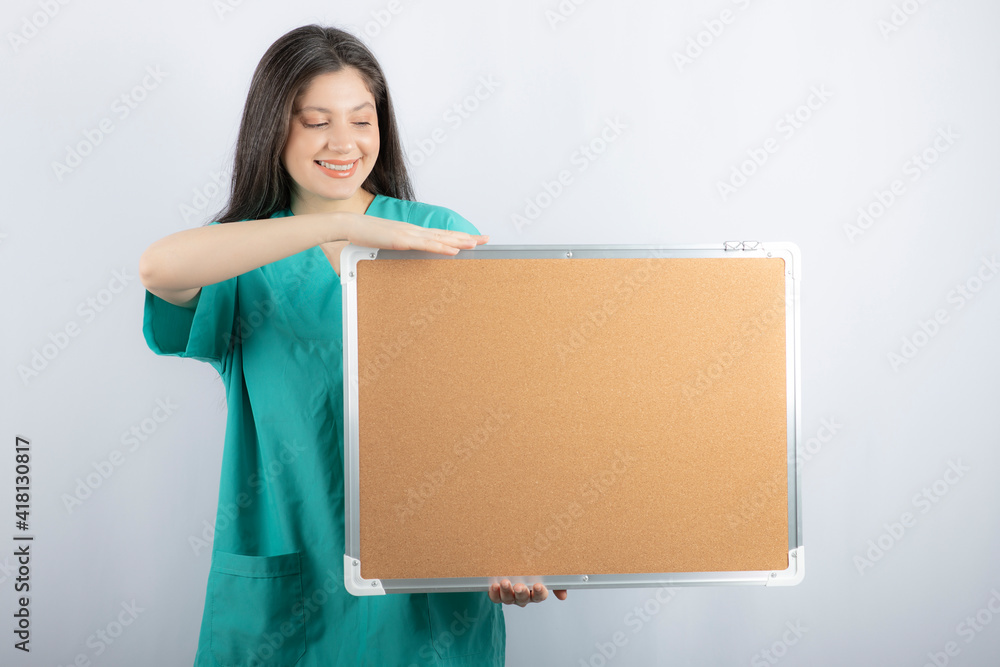 Smiling medical worker holding board and pointing finger on it Smiling medical worker holding board and pointing finger on it