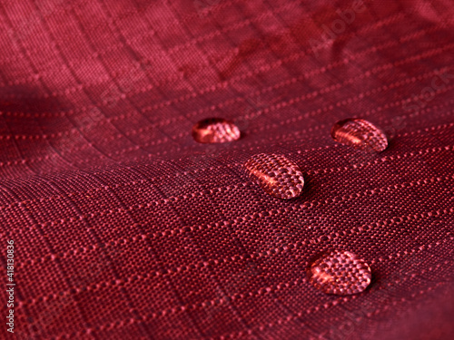 Water drops on waterproof membrane fabric. Detail view of texture of red waterproof cloth.