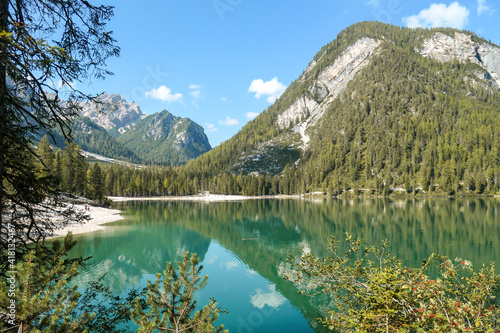 Fototapeta Naklejka Na Ścianę i Meble -  A view on the Pragser Wildsee, a lake in South Tyrolean Dolomites. High mountain chains around the lake. The sky and mountains are reflecting in the lake. Dense forest at the shore. Autumn vibe. Relax