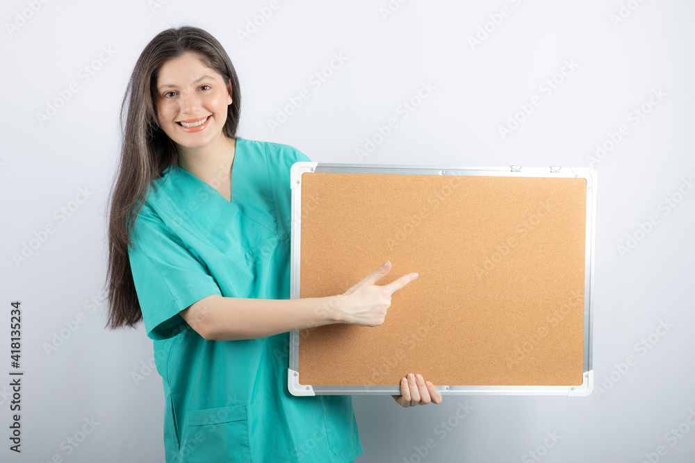 Smiling medical worker holding board and pointing finger on it Smiling medical worker holding board and pointing finger on it