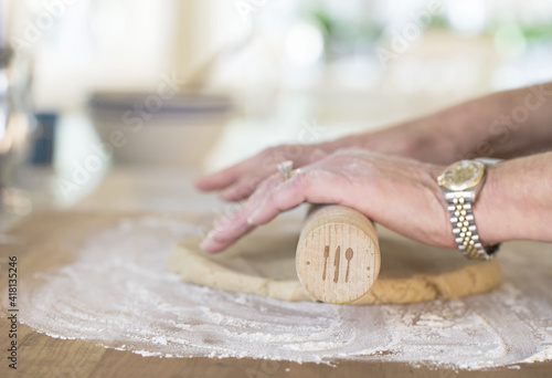 Original lifestyle photograph of a woman's hands rolling out dough in the kitchen with a rolling pin