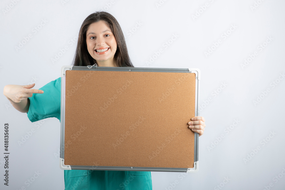 Smiling young woman holding board and pointing finger on it Smiling young woman holding board and pointing finger on it