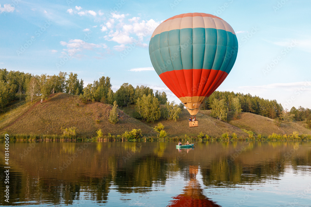 Obraz premium hot air balloon over the river, a boat is sailing along the river