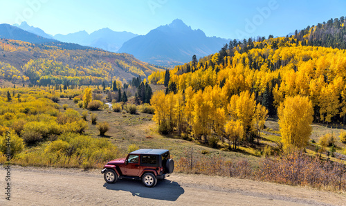 Autumn Valley - A red SUV exploring in a colorful valley at base of rugged Sneffels Range on a bright sunny Autumn morning. Ridgway-Telluride, CO, USA. photo