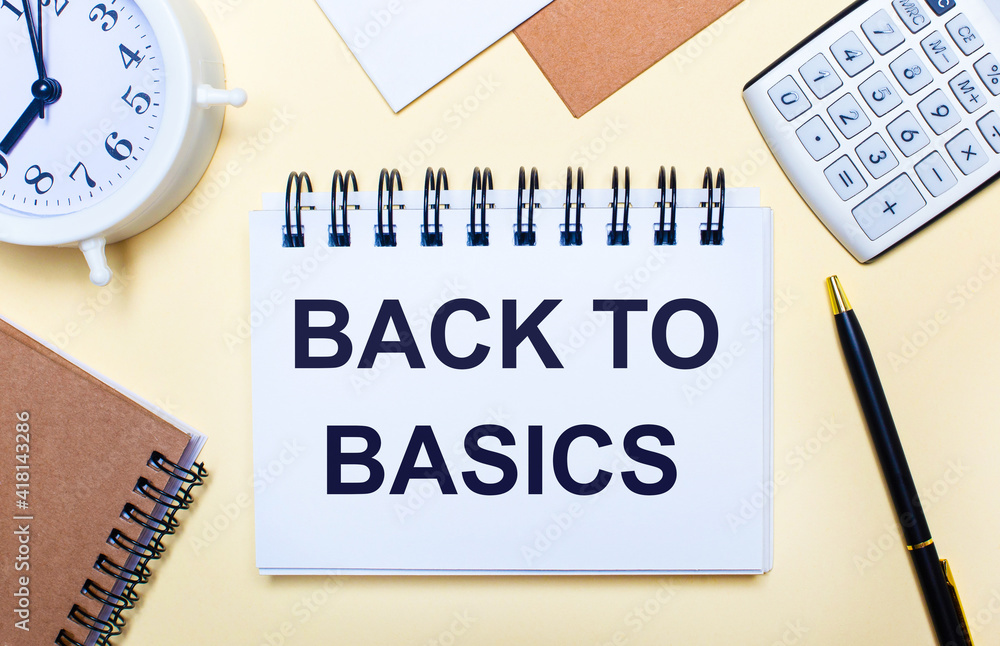On a light background, a white alarm clock, a calculator, a pen and a notebook with the text BACK TO BASIC On a light background, a white alarm clock, a calculator, a pen and a notebook with the text BACK TO BASIC