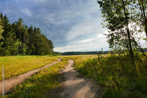 Rural landscape in warm colors. Simnye clouds and a green field along which the road passes. Poster or postcard. Background for your design.