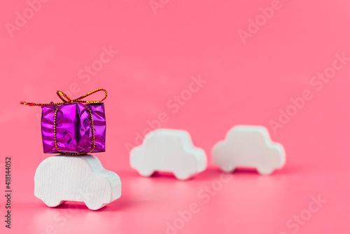 Gift delivery concept. Toy car delivers gift box on pink background. February 14 postcard, Valentine's Day, Christmas, New year, March 8, international women's day. Minimalism style.