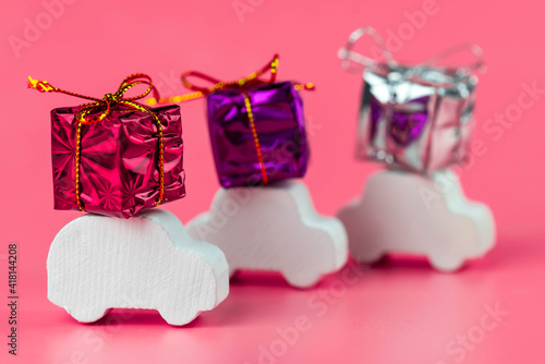 Gift delivery concept. Toy car delivers gift box on pink background. February 14 postcard, Valentine's Day, Christmas, New year, March 8, international women's day. Minimalism style.