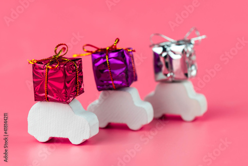 Gift delivery concept. Toy car delivers gift box on pink background. February 14 postcard, Valentine's Day, Christmas, New year, March 8, international women's day. Minimalism style.