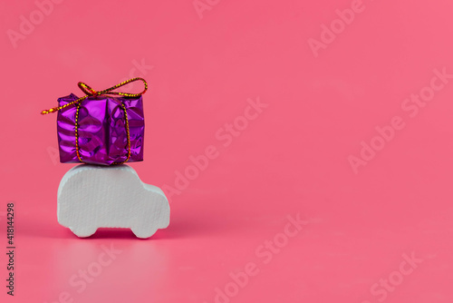 Gift delivery concept. Toy car delivers gift box on pink background. February 14 postcard, Valentine's Day, Christmas, New year, March 8, international women's day. Minimalism style.