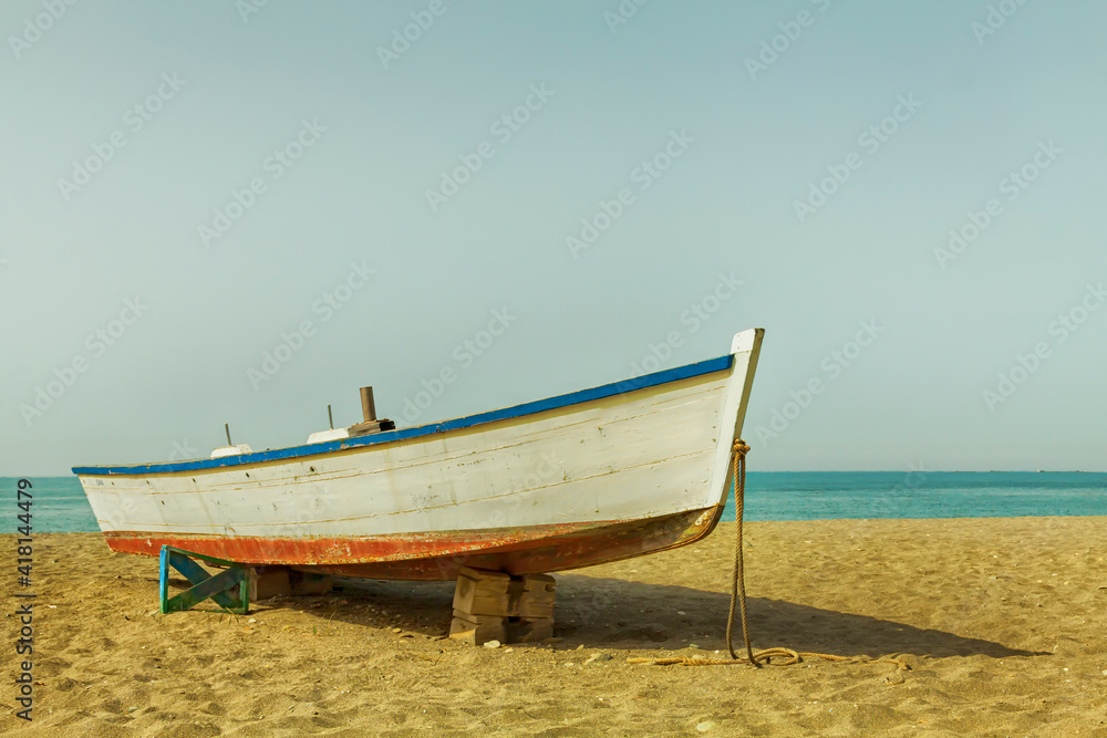 A small wooden boat used by fishermen beached on the sandy beach next to the Mediterranean Sea