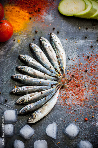Small fresh sea fish lies on a dark background with bright spices