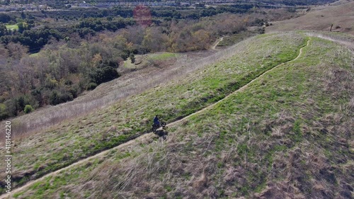 Aerial rotating drone view of a man riding his bike on a desolate ridge trail on a sunny day photo