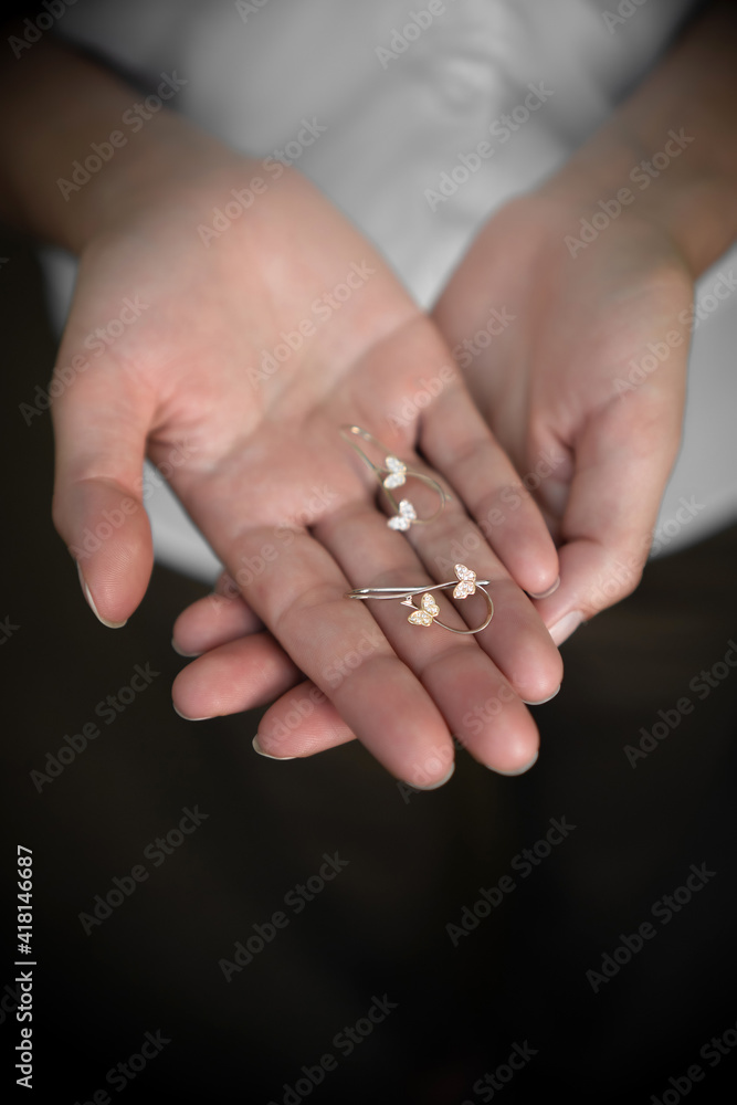 Earrings in woman's hands on dark background, hands, fingers Earrings in woman's hands on dark background, hands, fingers