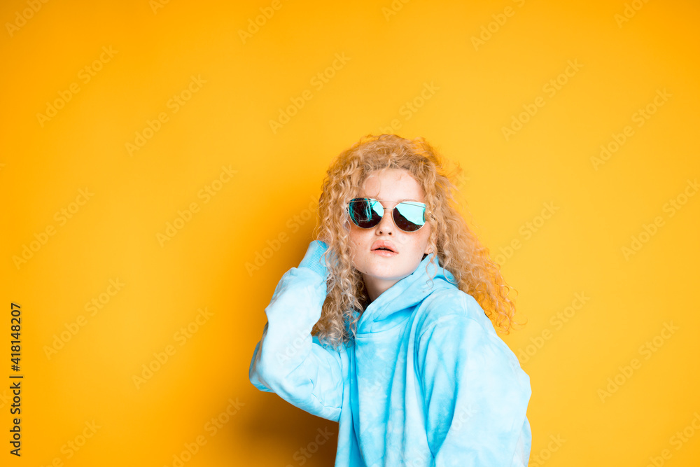 Charming woman with curly blonde hair in a blue sweater with glasses pulls back a lock of hair Charming woman with curly blonde hair in a blue sweater with glasses pulls back a lock of hair
