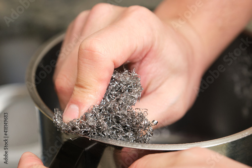 Obraz na plátně Cropped image of a man hands washing a pot or doing the dishes with a stainless steel sponge scrubber