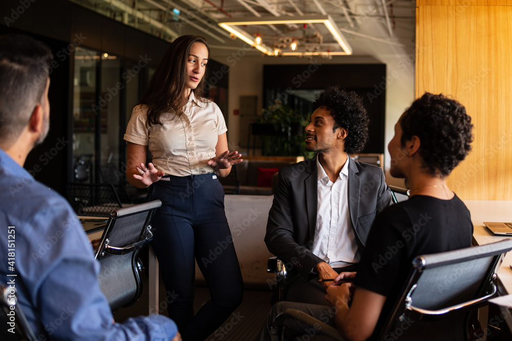 Obraz premium brazilian woman talking causally with co-workers.in workstation. .