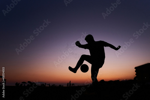 Silhouette of young man playing soccer on the beach with a ball at sunset