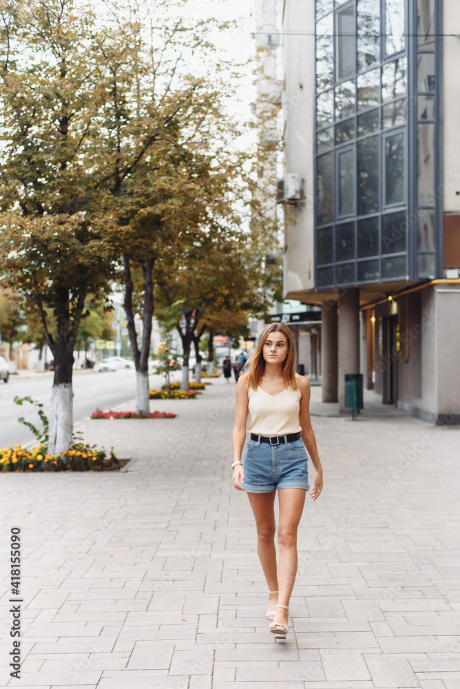 Summer sunny lifestyle fashion portrait of young stylish hipster woman walking on the street, wearing cute trendy outfit, smiling enjoy her weekends
