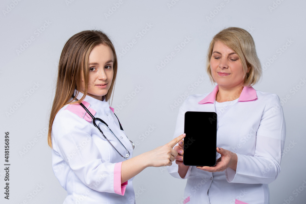 Happy women, professional nurses, female doctors wear white uniform show digital tablet mock up blank empty screen advertise medical care app tech concept isolated on gray studio background. Happy women, professional nurses, female doctors wear white uniform show digital tablet mock up blank empty screen advertise medical care app tech concept isolated on gray studio background.