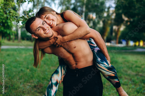 Happy, athletic girl jumped on the guy's back. Young, loving couple outdoors. Sport is a way of life.