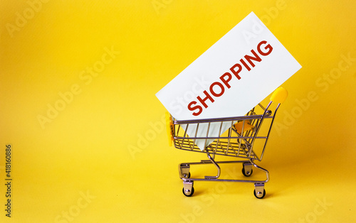 image of a miniature shopping trolley, inside the trolley sticker with the text SHOPPING, on a yellow background