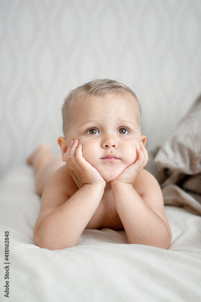 Portrait of a little handsome boy lying on the bed, holding his head with his hands and looking in front of him. Vertical frame. Portrait of a little handsome boy lying on the bed, holding his head with his hands and looking in front of him. Vertical frame.