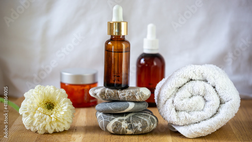 Organic natural cosmetic set of essential oil products for skin care and beauty. Bottle balancing on stacked stones.  Hand towel, white flower as decoration on a wooden table. Balance restore concept.