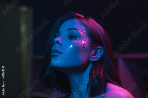 Tableau sur toile Close photo of a beautiful woman with bright makeup at a night party with purple and blue light, looking away with a serious face