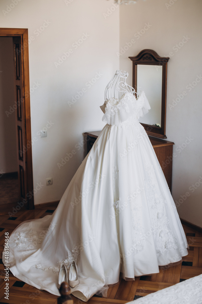 Delicate white dress of the bride on a white mannequin and on spaghetti straps in the bride's room near the window